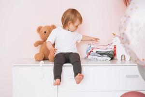 Cute funny baby girl happy child in home clothes sitting on commode at home photo