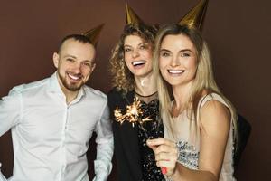 des gens heureux portant des chapeaux de fête tenant des étincelles brûlantes pendant les vacances ou la célébration d'un événement photo