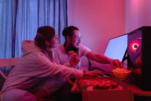 couple se détendre à la maison dans la chambre avec néon et manger de la pizza, regarder des films en ligne ou jouer à des jeux vidéo photo