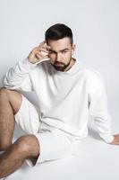 bel homme portant un sweat-shirt blanc et un short avec des écouteurs sans fil assis photo