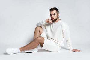 bel homme portant un sweat-shirt blanc et un short avec des écouteurs sans fil assis photo