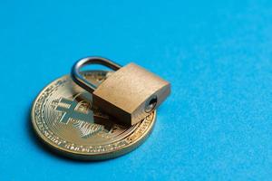 petit cadenas en laiton sur un bitcoin doré brillant sur fond bleu. photo