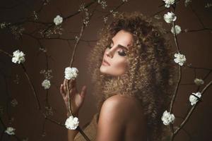 jolie jeune femme avec une coiffure afro et un beau maquillage avec beaucoup de fleurs blanches photo