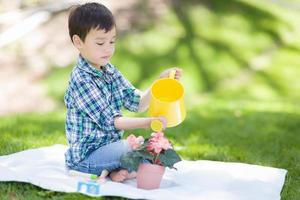 jeune garçon de race mixte arrosant ses fleurs en pot à l'extérieur sur l'herbe photo