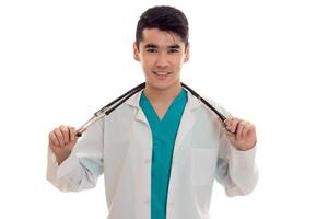 heureux médecin élégant en uniforme bleu avec stéthoscope posant et regardant la caméra isolée sur fond blanc photo