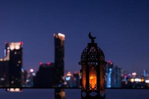 lanterne qui a le symbole de la lune sur le dessus avec un fond de ville nocturne pour la fête musulmane du mois sacré du ramadan kareem. photo