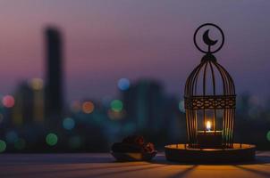 lanterne qui a le symbole de la lune sur le dessus et une petite assiette de fruits de dattes avec ciel crépusculaire et fond clair bokeh de la ville pour la fête musulmane du mois sacré du ramadan kareem. photo