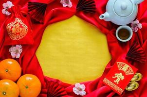 dîner du nouvel an chinois avec service à thé, paquet d'enveloppe rouge ou mot ang bao signifie félicitations, lingots, oranges et mot de sac rouge signifient richesse sur tissu de satin rouge avec fond d'espace doré. photo