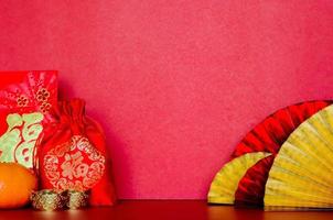 sélectif sur le mot de sac rouge signifie la richesse avec des paquets d'enveloppe ou le mot ang bao signifie la richesse, les lingots et l'orange avec des éventails orientaux dorés et rouges sur fond rouge pour le concept du nouvel an chinois. photo