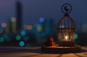 lanterne qui a le symbole de la lune sur le dessus et les fruits des dates mis sur un plateau en bois avec des lumières colorées de bokeh de la ville pour la fête musulmane du mois sacré du ramadan kareem. photo