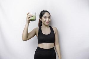 joyeuse femme asiatique sportive portant des vêtements de sport avec un verre de smoothie vert savoureux, isolé sur fond blanc. photo