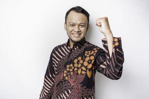 un jeune homme asiatique avec une expression heureuse et réussie portant une chemise batik isolée par fond blanc photo