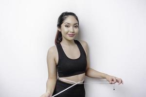 portrait d'une jeune femme asiatique joyeuse en vêtements de sport mesurant la taille avec du ruban adhésif, se sentant heureuse de perdre du poids à la maison. concept de mode de vie sain, de sport et de régime amincissant photo