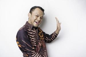 homme asiatique excité portant une chemise batik pointant vers l'espace de copie à côté de lui, isolé sur fond blanc photo