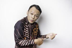 homme asiatique choqué portant une chemise batik pointant vers l'espace de copie à côté de lui, isolé sur fond blanc photo