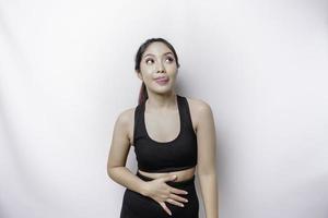 une femme asiatique sportive a faim et touche son ventre tout en regardant de côté en pensant quoi manger photo