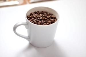 mug gris clair rempli de fèves de cacao sur fond clair. le concept de boire beaucoup de caféine photo