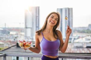 commencer la journée avec des aliments sains. jeune et belle femme appréciant une salade saine avec du soleil derrière elle. régime équilibré. belle femme souriante mangeant une salade végétarienne bio fraîche. photo