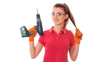 belle jeune femme aux cheveux noirs en uniforl fait des rénovations avec une perceuse dans ses mains isolé sur fond blanc photo