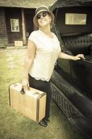 bonne fille habillée des années 1920 tenant une valise à côté d'une voiture d'époque photo