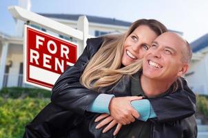 couple heureux serrant devant l'enseigne et la maison à louer de l'immobilier photo