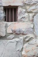 vieux mur de pierre avec une petite fenêtre de cellule de prison à barreaux de fer photo