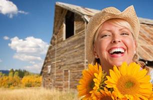 belle jeune femme caucasienne portant un chapeau de cow-boy tenant un tournesol devant une grange rustique dans le pays. photo