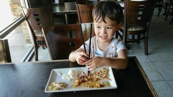 mignon jeune garçon chinois et caucasien apprenant à utiliser des baguettes au restaurant photo