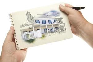 mains tenant un stylo et un bloc de papier avec un dessin de maison photo