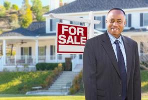 agent afro-américain devant une belle maison personnalisée et une enseigne immobilière à vendre. photo