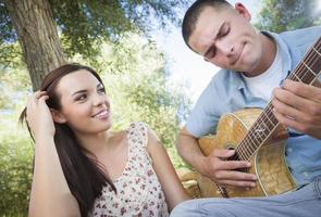 couple de race mixte au parc jouant de la guitare et chantant photo