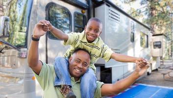 heureux père et fils afro-américains devant leur beau camping-car au camping. photo