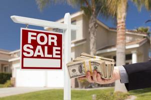 Acheteur remettant de l'argent pour une maison avec un panneau à vendre