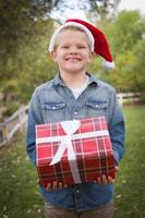 jeune garçon portant des vêtements de vacances tenant un cadeau de noël à l'extérieur photo