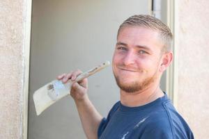 jeune homme caucasien souriant alors qu'il peint la maison photo