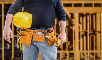 entrepreneur avec ceinture à outils et casque de sécurité devant le chantier de construction à ossature bois photo