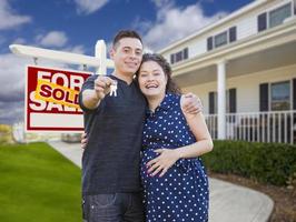 couple hispanique avec clés devant la maison et signe photo