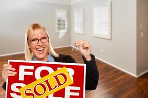 femme avec vendu à vendre signe immobilier et clés dans la salle vide de la nouvelle maison photo