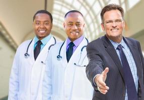 médecins de race mixte derrière un homme d'affaires qui tend la main pour serrer la main à l'intérieur de l'hôpital photo