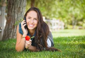 Attractive happy mixed race young female talking on cell phone à l'extérieur portant dans l'herbe photo