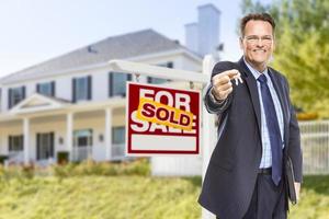 agent avec clés devant l'enseigne et la maison vendues photo