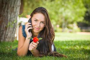 Attractive happy mixed race young female talking on cell phone à l'extérieur portant dans l'herbe photo