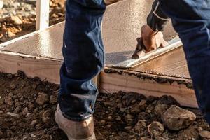 travailleur de la construction à l'aide d'une truelle en bois sur du ciment humide faisant face autour d'une nouvelle piscine photo