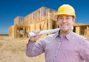 entrepreneur souriant portant un casque tenant des plans sur le chantier de construction de la maison. photo