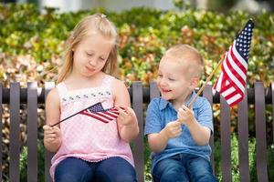 jeune soeur et frère comparant la taille du drapeau américain sur le banc du parc photo