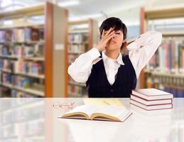 jeune étudiante métisse stressée et frustrée dans la bibliothèque avec un bloc-notes vierge et des livres. photo