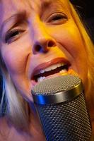 la chanteuse sous un éclairage gélifié chante avec passion dans un microphone à condensateur. photo