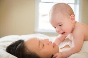 Mixed Race Chinese and Caucasian baby boy portant au lit avec sa mère photo