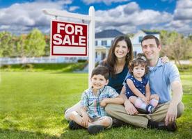 jeune famille avec enfants devant une maison personnalisée et une enseigne immobilière à vendre. photo