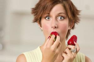 jolie femme aux cheveux rouges aux yeux écarquillés mordant la fraise photo